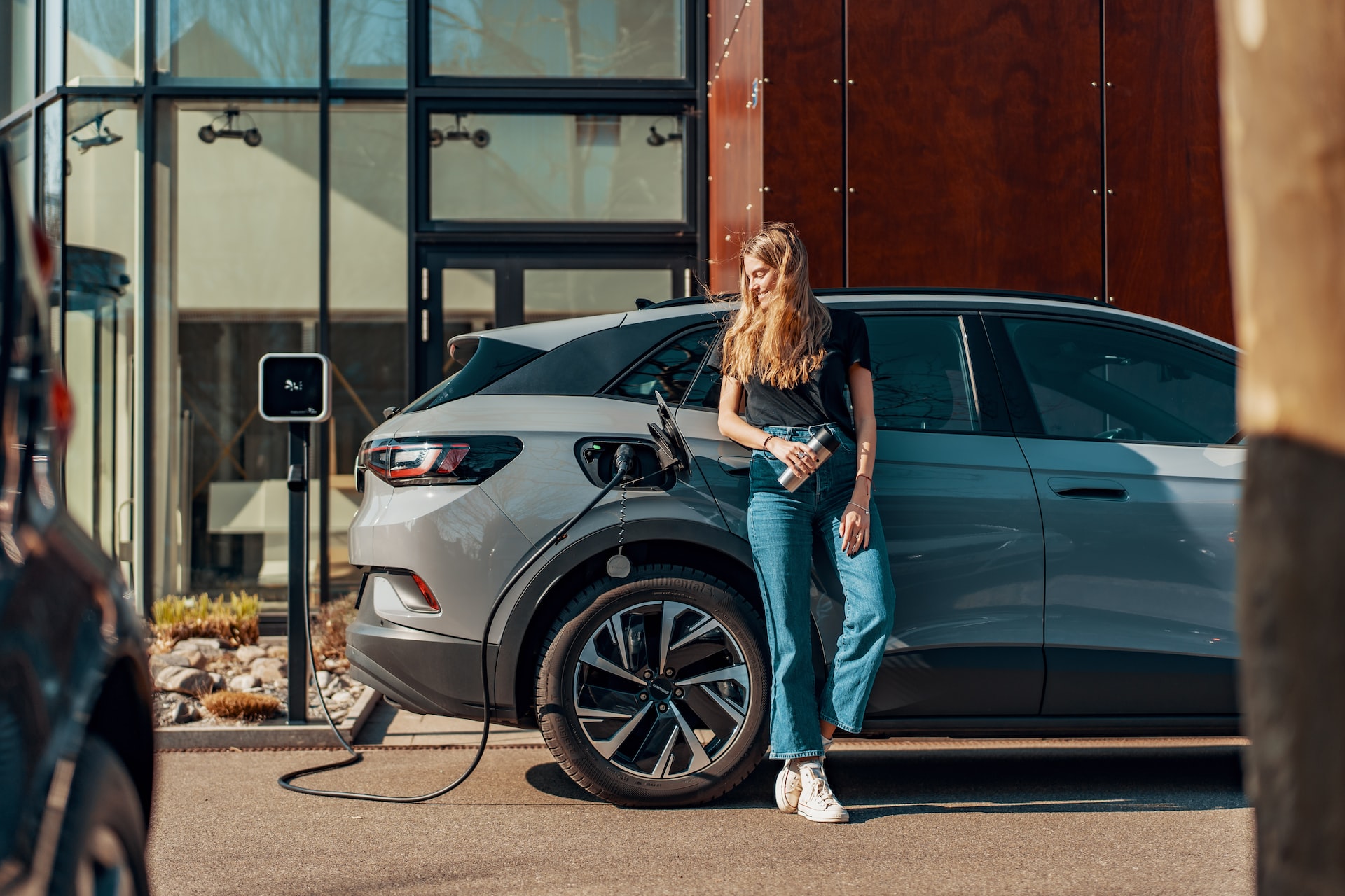 A woman standing next to car at a charging station.